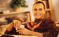 Fotografía de un hombre joven y sonriente, sosteniendo una taza de café