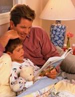 Fotografía de un padre que escucha a su hijo leer un libro antes de dormir