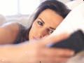 Mujer infeliz en la cama mirando a su teléfono celular