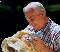 Fotografía de un abuelo cargando a su nieto recién nacido, la alimentación de él una botella